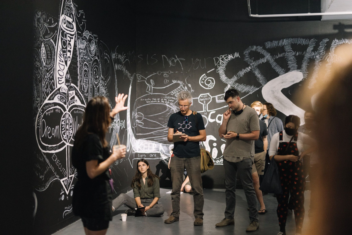 Audience listens actively as artist Giselle Stanborough speaks animatedly inside the gallery space.