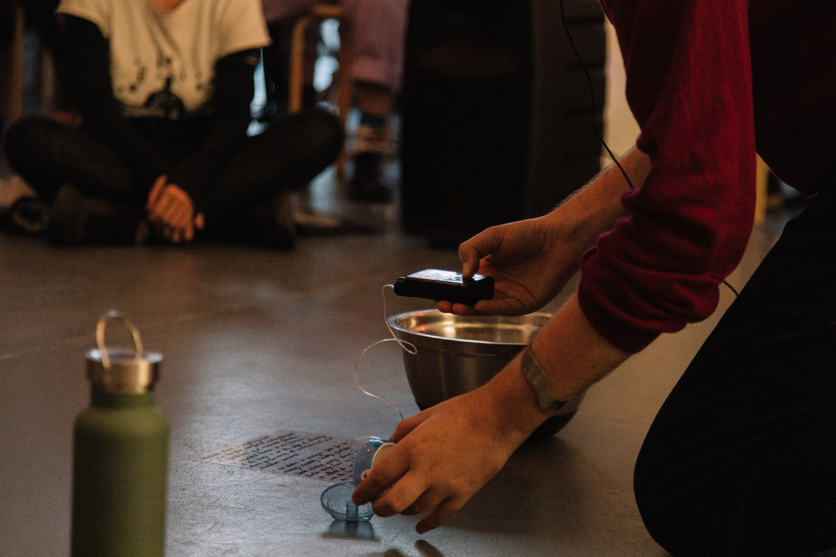 A man kneels in front of audience, a small device in his hand.