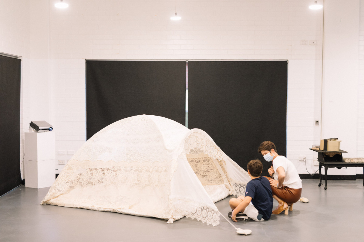 Two people squat to look into a tent made of lace.