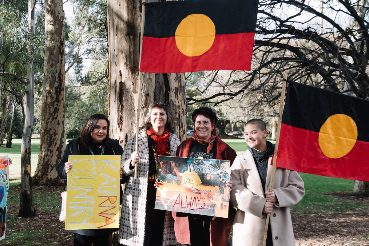 Jayda Wilson, Tikari Rigney and two members of Unbound Collective hold protest poster and Aboriginal flags in a park.