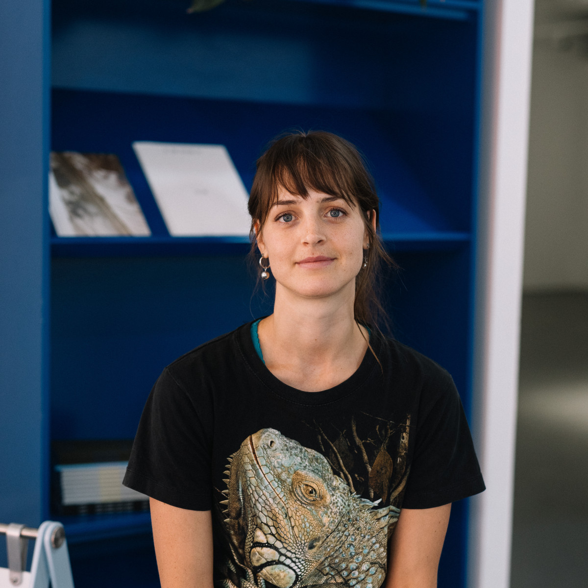 Emmaline Zanelli headshot. Zanelli smiles to camera, she is sitting in front of a blue bookcase.