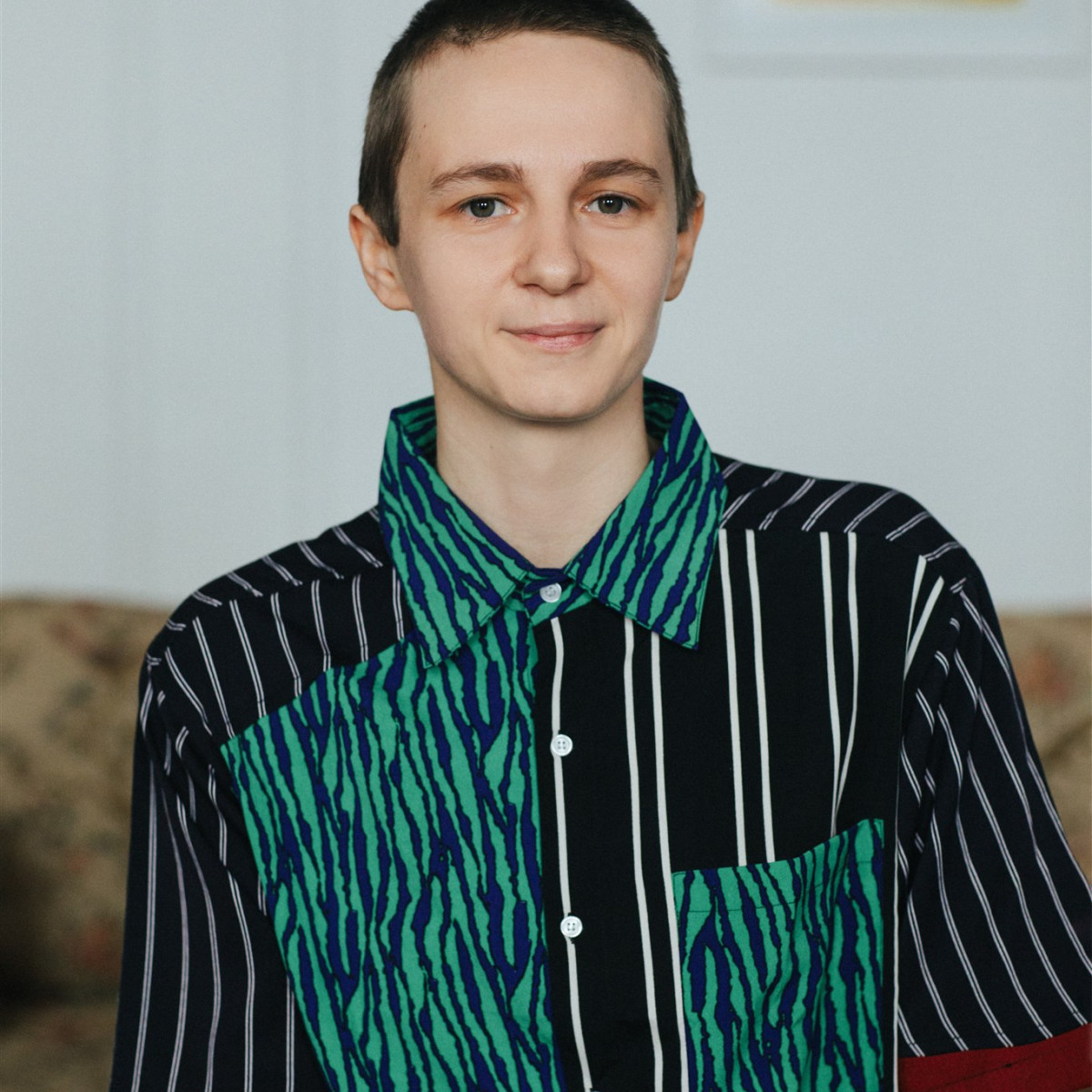 Headshot of Finnegan Shannon. Me, a white person with close-cropped hair. Here with a reserved smile and my most fun shirt (a multi-patterned, asymmetrical button-up)