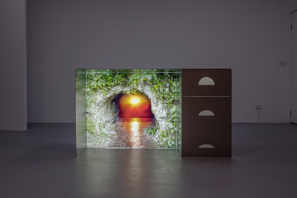 A large object sits in the centre of a dimply lit exhibition space. The object features a sunset motif surrounded by a cave-like situation.