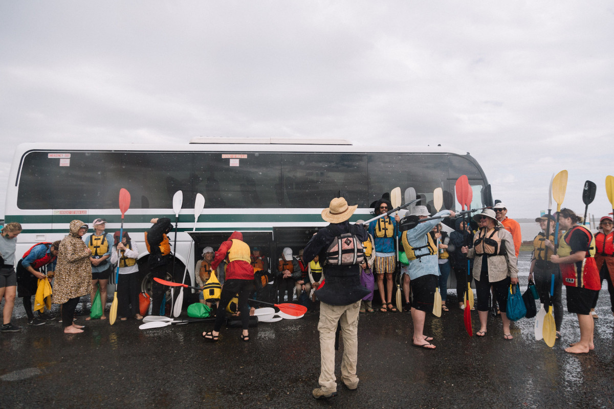 Group stands by the bus with their paddles. It's raining.