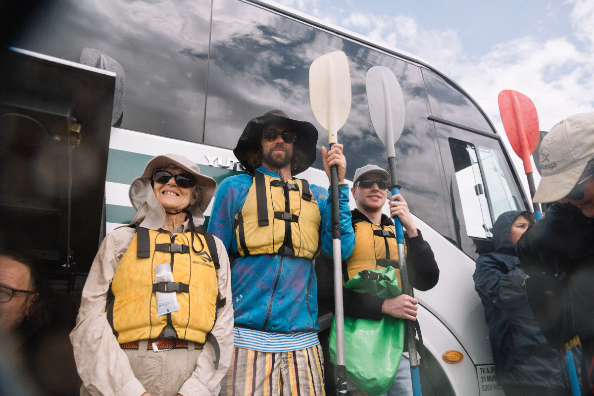 Three people stand by the bus with their paddles.