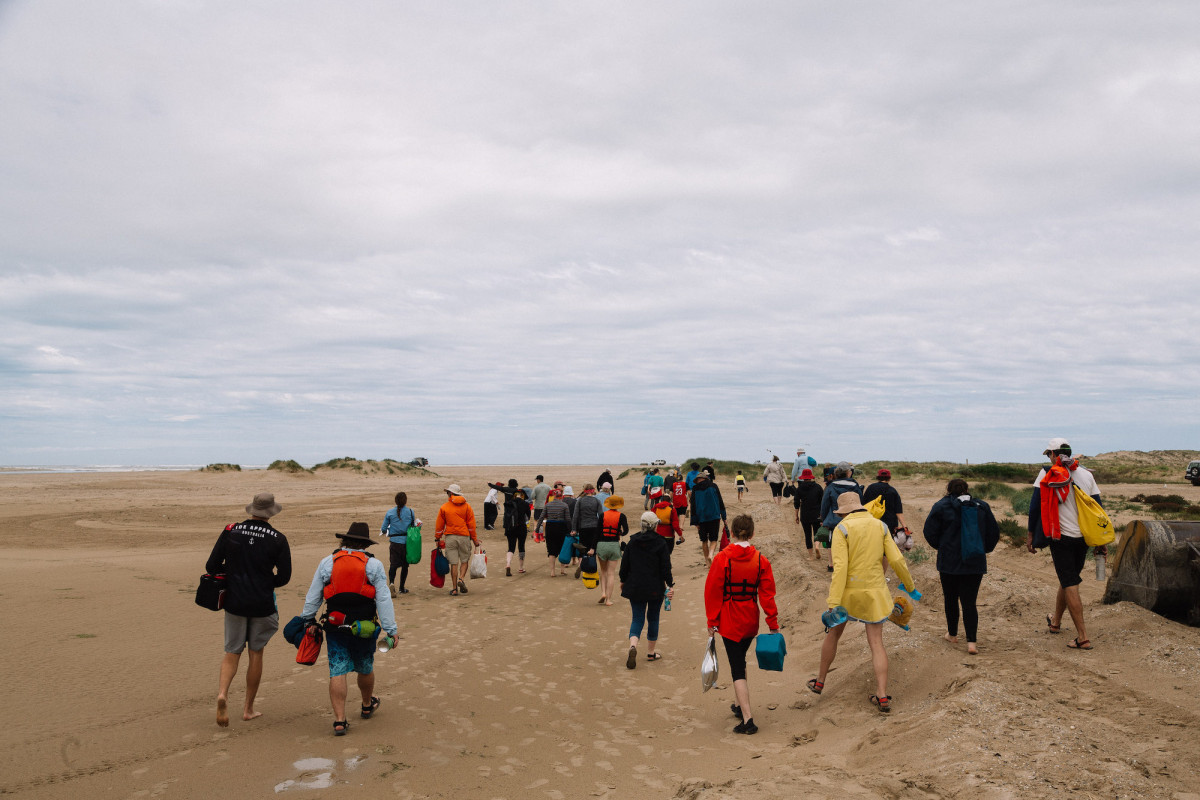 Group walks on the beach with bags and drink bottles in hand.
