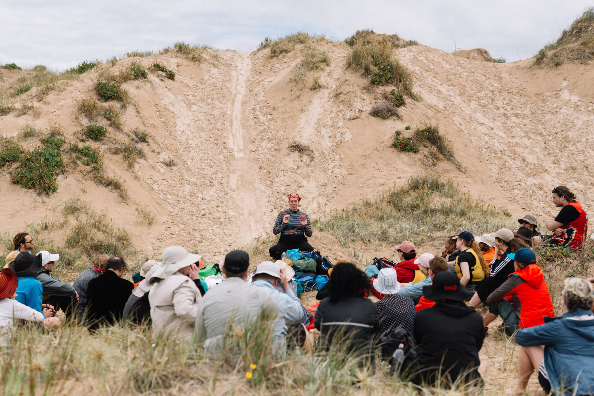 Group gathers around Tikari Rigney in the dunes.
